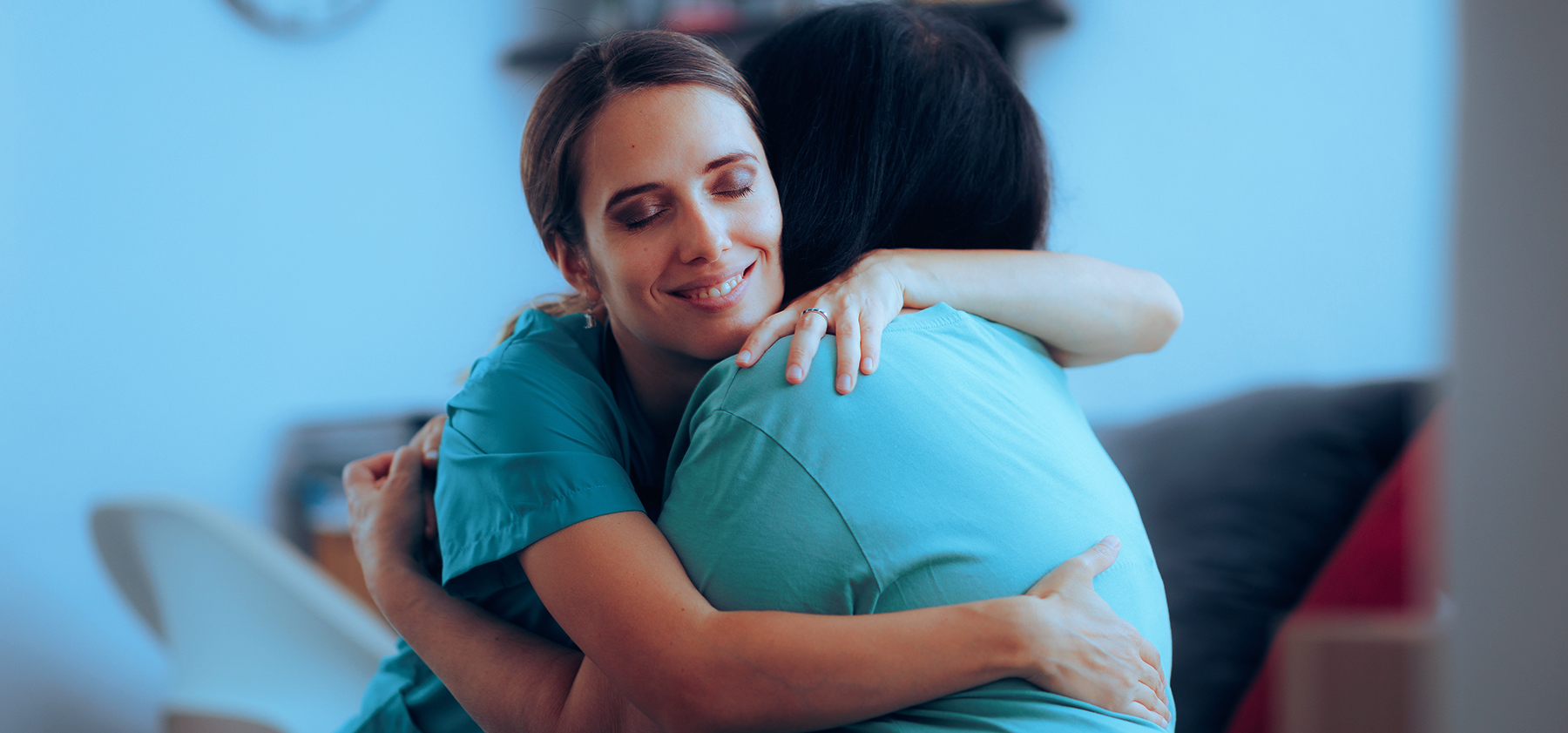 Two female caregivers wearing scrubs embracing to show affection